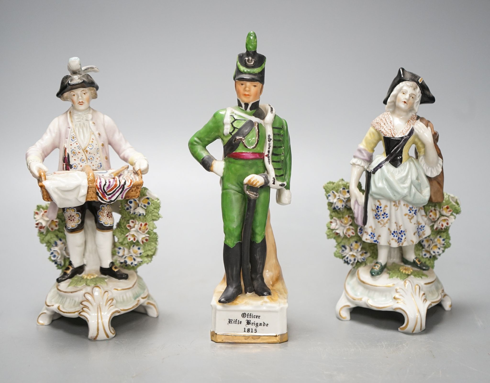 A pair of Dresden porcelain figures of a street-trader and companion and a continental porcelain figure of a Rifle Brigade officer (3) 19.5cm